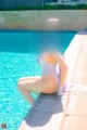 A woman in a white bathing suit sitting by a swimming pool.